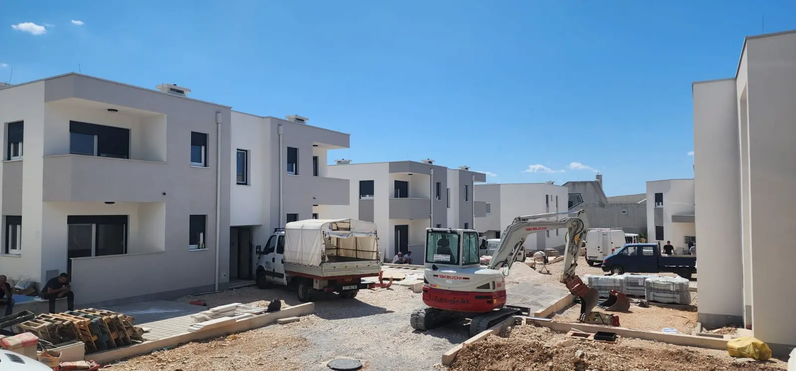 Gradilište Archicon Split s modernim stambenim zgradama i bagerom Takeuchi pod vedrim nebom.