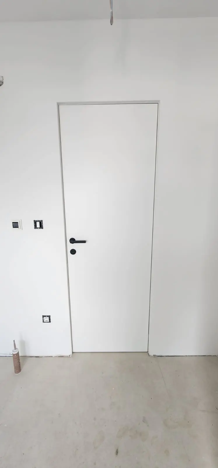Bijela unutarnja vrata s crnom kvakom i okviri za utičnice u interijeru Archicon Split.