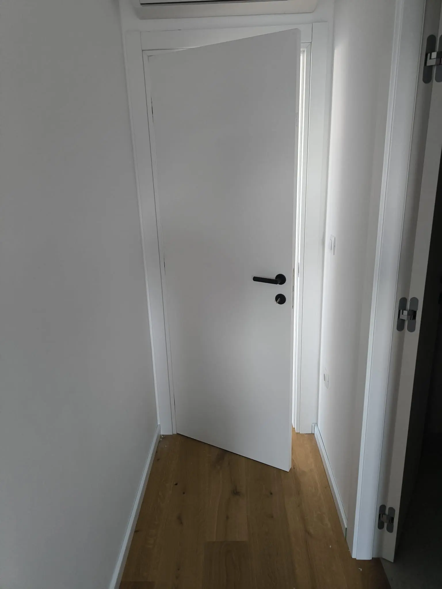 Bijela unutarnja vrata s crnom kvakom i drvenim podom, moderni interijer Archicon Split.