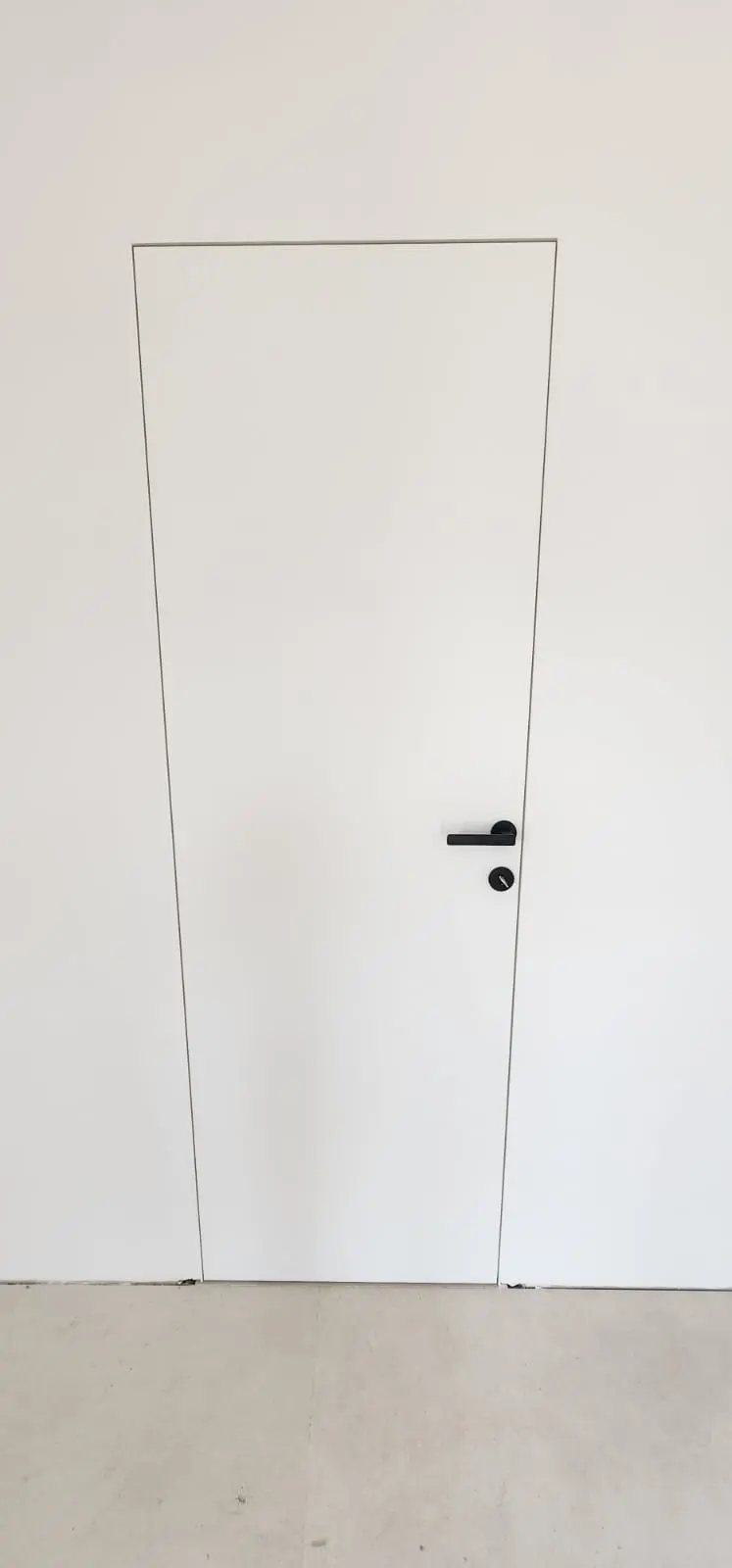 Moderna bijela vrata u ravnini zida s crnom kvakom, minimalistički dizajn Archicon Split.