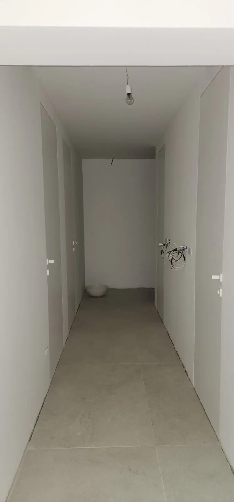 Hodnik u izgradnji s bijelim zidovima, sivim pločicama i golom žaruljom, Archicon Split