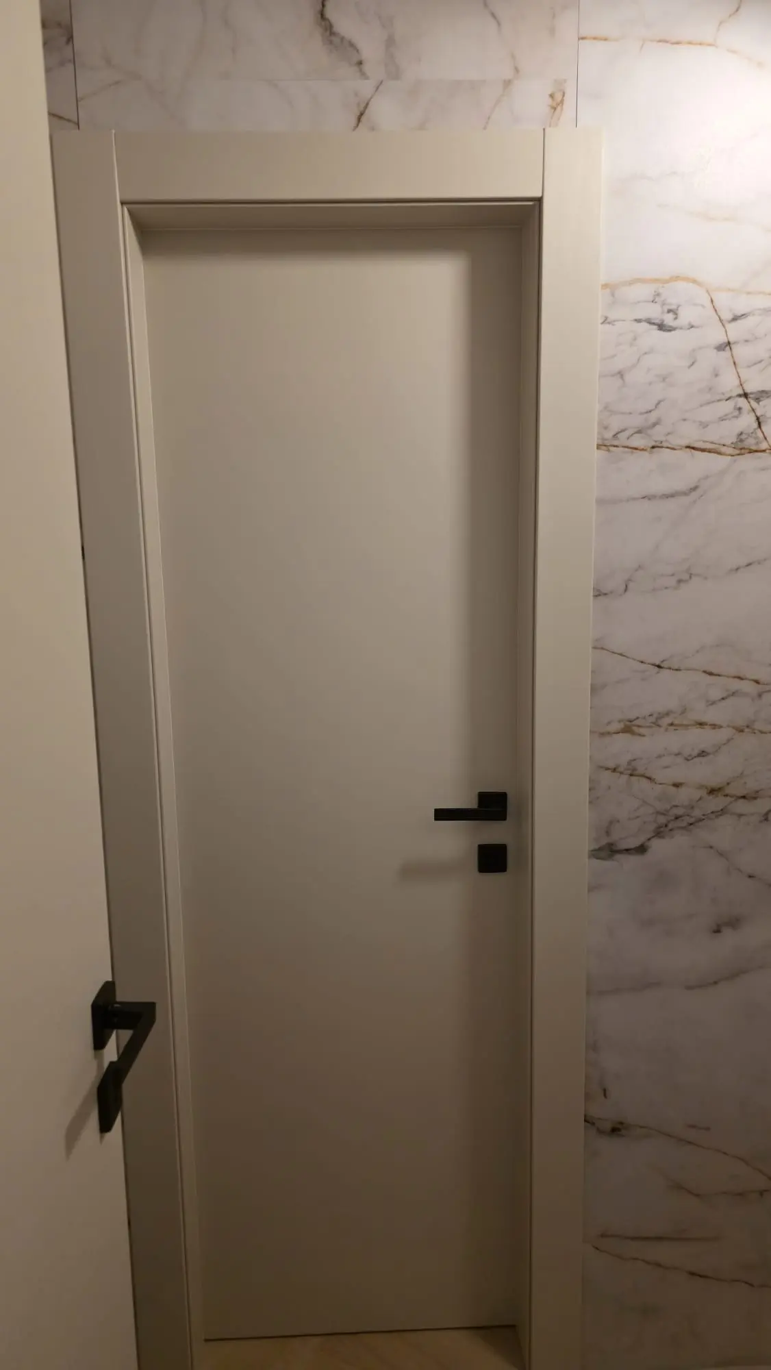 Moderna bijela vrata s crnom kvakom uz zid od bijelog mramora s zlatnim žilama, Archicon Split.