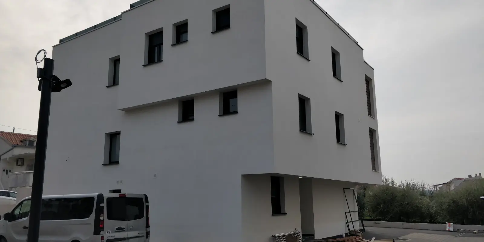 Moderna bijela zgrada Archicon Split s tamnim prozorima, srebrnim kombijem i uličnom rasvjetom.