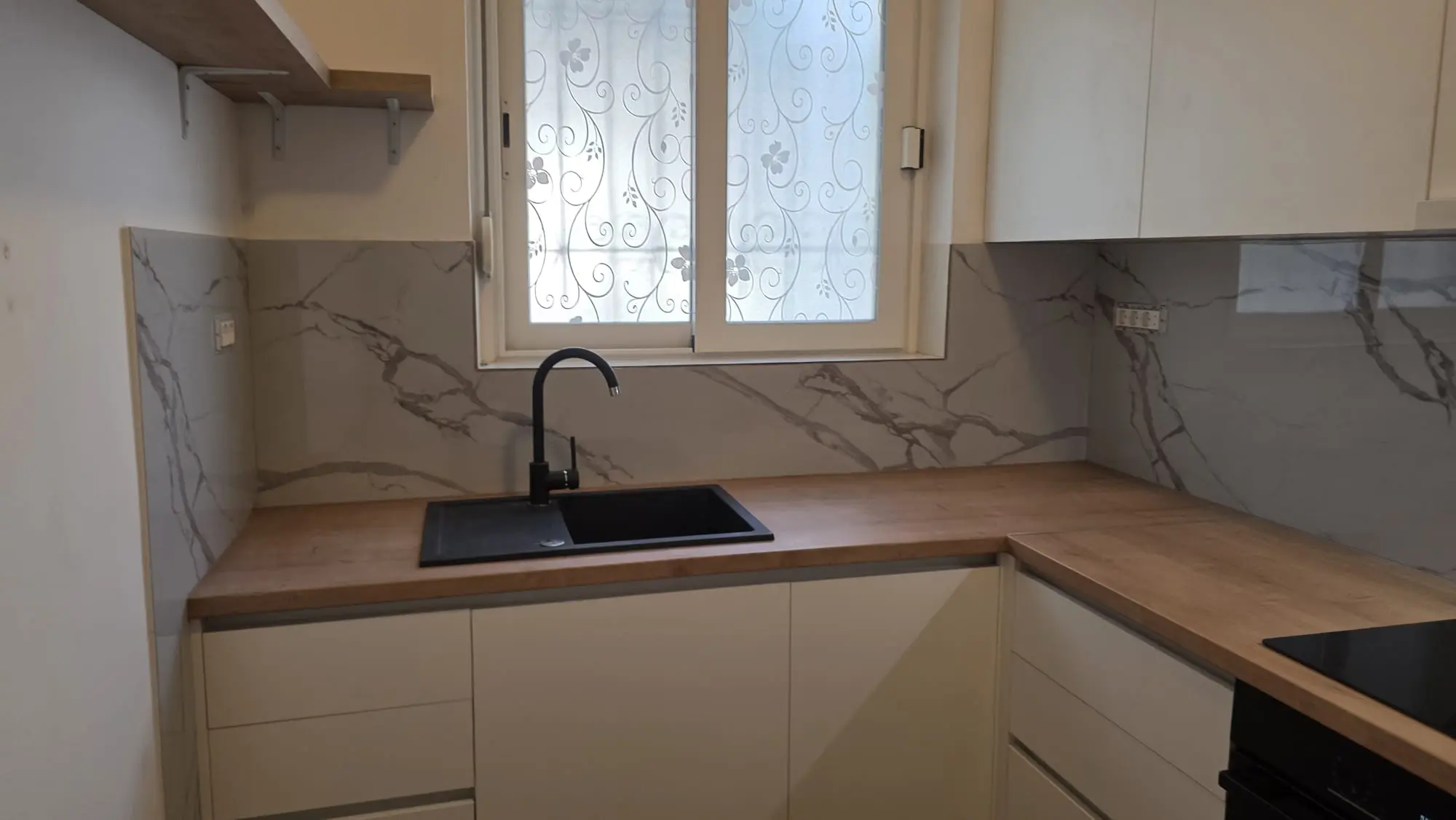 Moderna kuhinja Archicon Split s bijelim ormarićima, drvenom pločom, mramornim zidnim oblogama i crnim sudoperom.