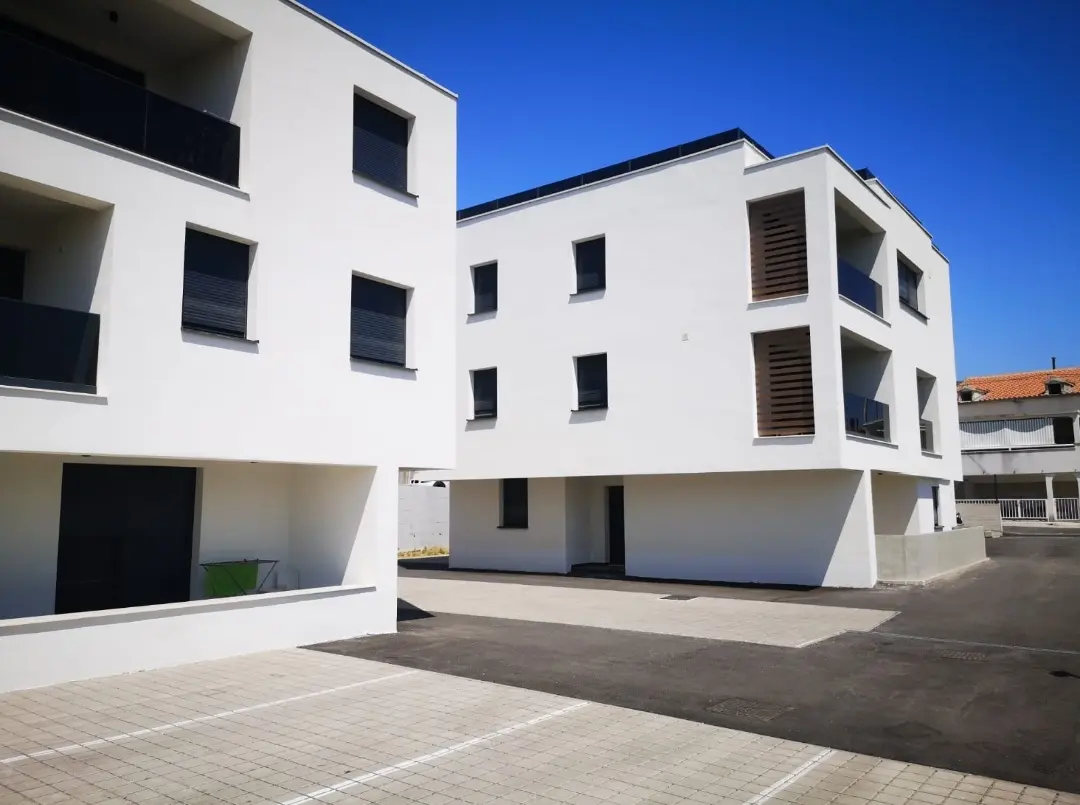Moderne bijele stambene zgrade Archicona s balkonima i parkiralištem pod vedrim nebom.