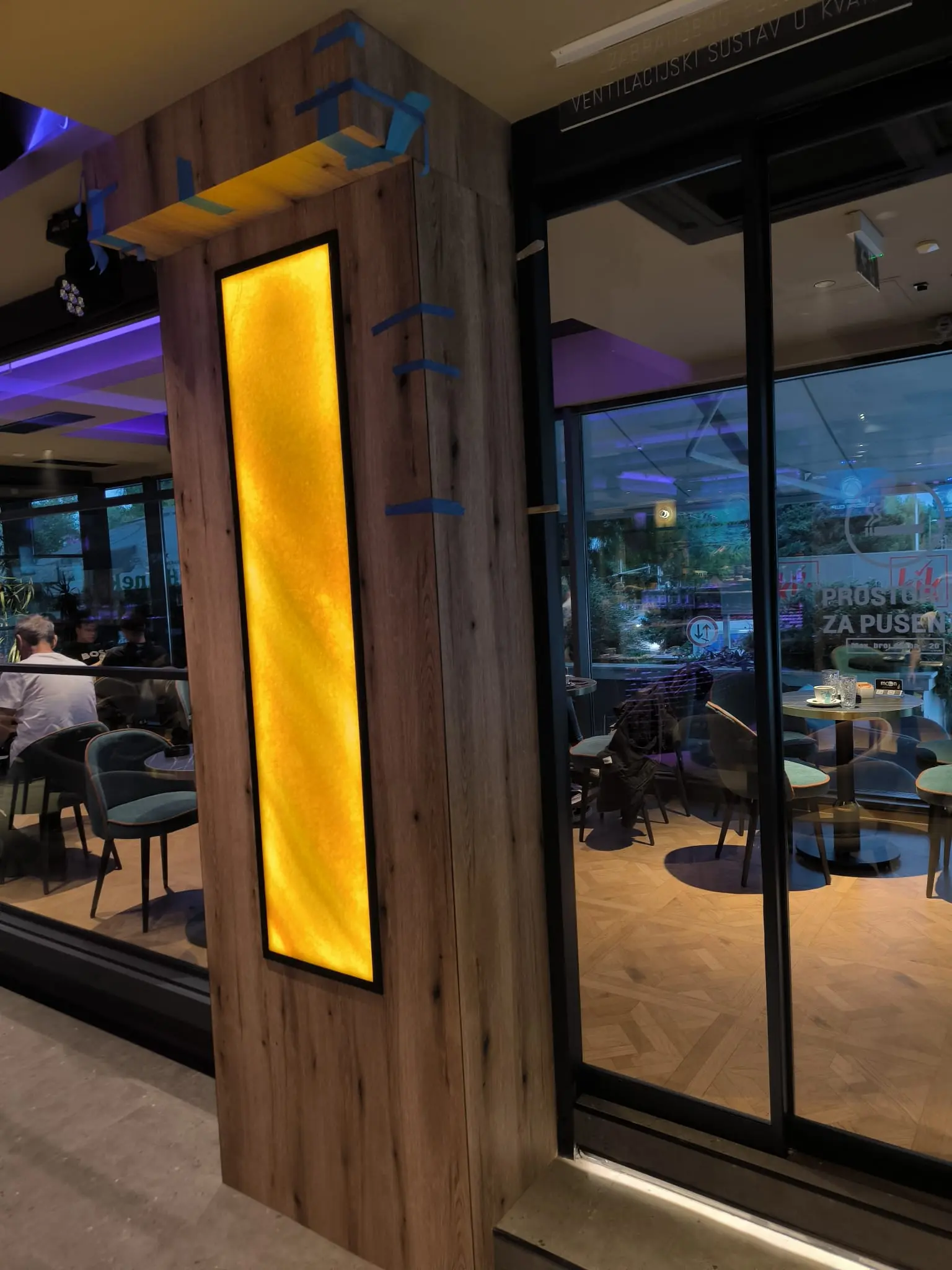 Moderan interijer kafića s drvenim stupom, žutim osvjetljenjem i staklenom fasadom, Archicon Split.