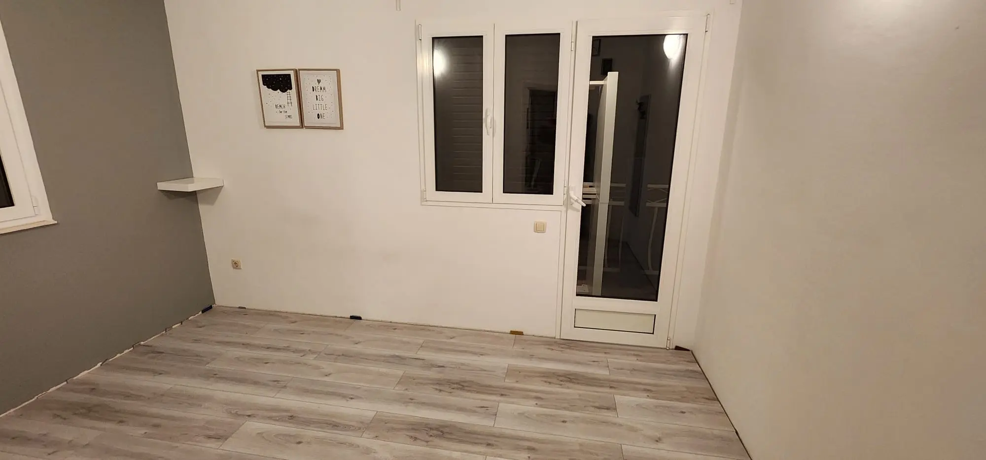 Prazna soba s laminatom, bijelim i sivim zidovima, prozorom i vratima, idealna za uređenje Archicon Split.