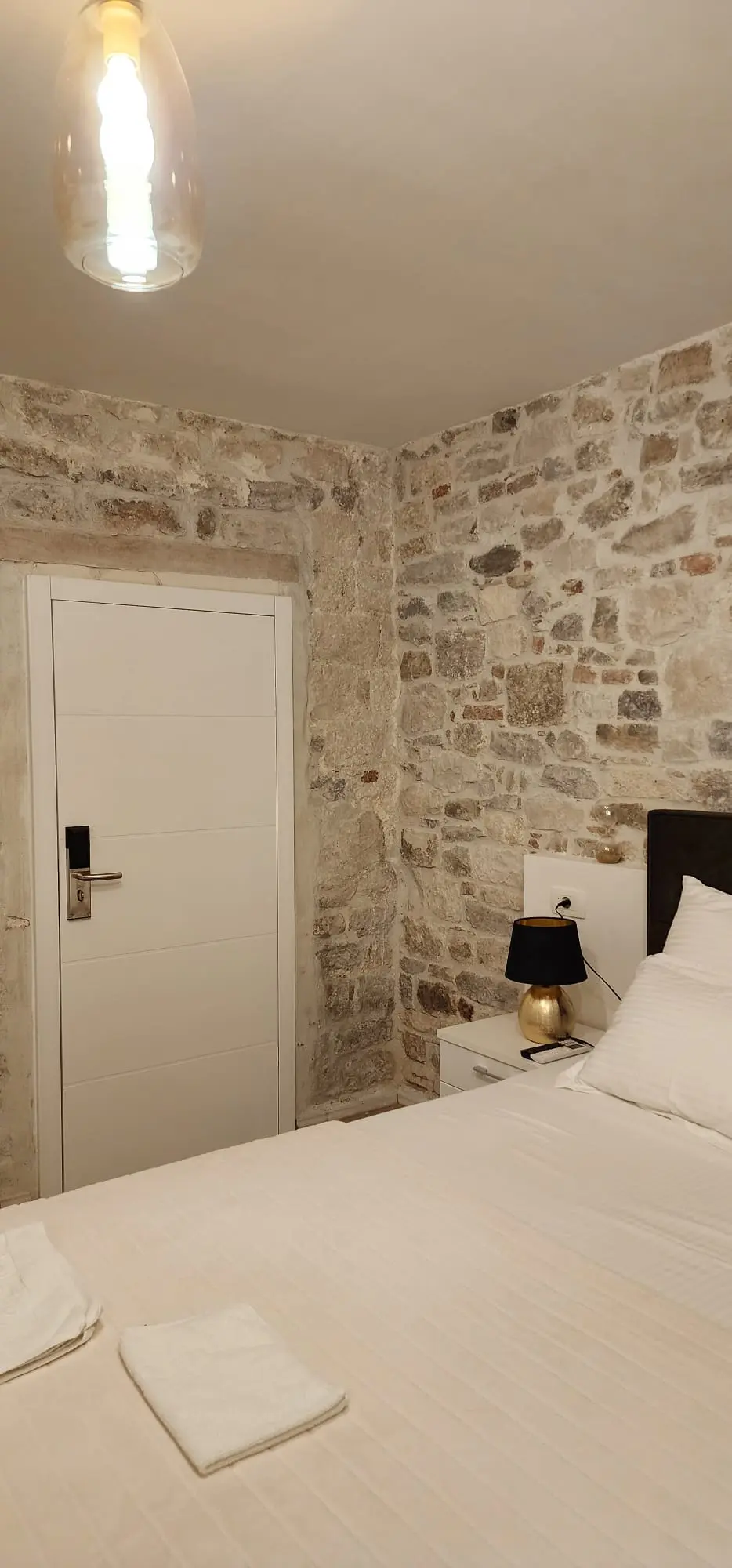 Udobna spavaća soba s kamenim zidovima, bijelim krevetom i modernim vratima, Archicon Split