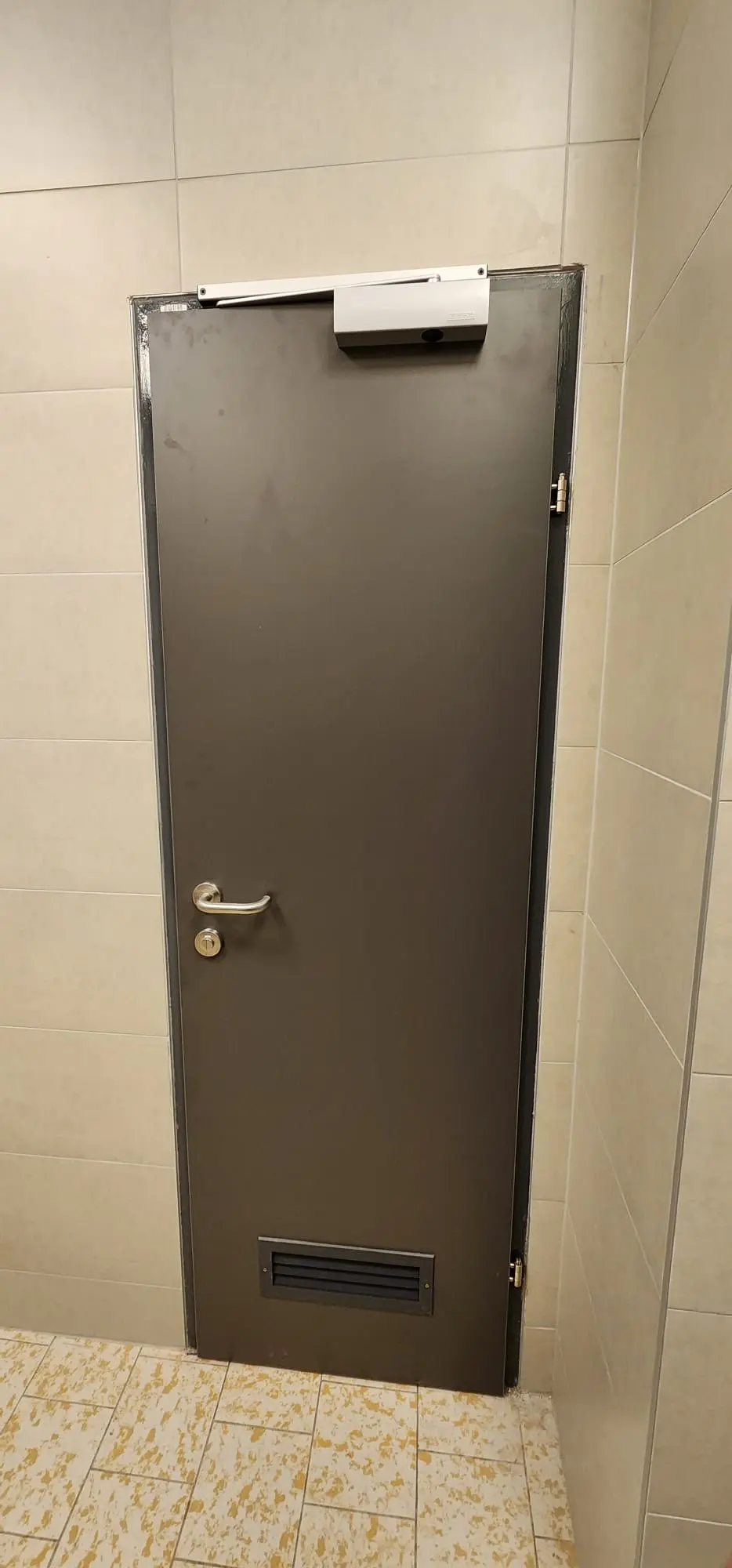 Tamna vrata s kvakom, zatvaračem i ventilacijskom rešetkom, okružena zidnim pločicama, Archicon